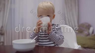 可爱的宝宝吃，喝牛奶。 小男孩喝玻璃牛奶。 快乐微笑的孩子，金发卷曲的孩子